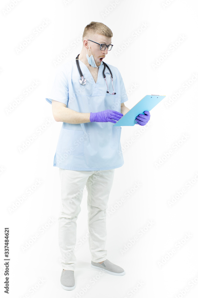 Young surprised male intern in uniform and mask looking shocked on clipboard with patient's medical diagnosis, isolated white background. Copy space. Prescription, hospital, medical, diseases concept Young surprised male intern in uniform and mask looking shocked on clipboard with patient's medical diagnosis, isolated white background. Copy space. Prescription, hospital, medical, diseases concept