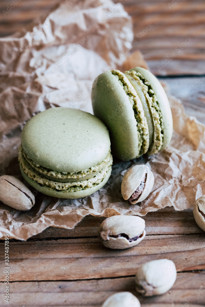 Deux macarons à la pistache et pistaches dans leur coque sur un fond bois naturel Deux macarons à la pistache et pistaches dans leur coque sur un fond bois naturel