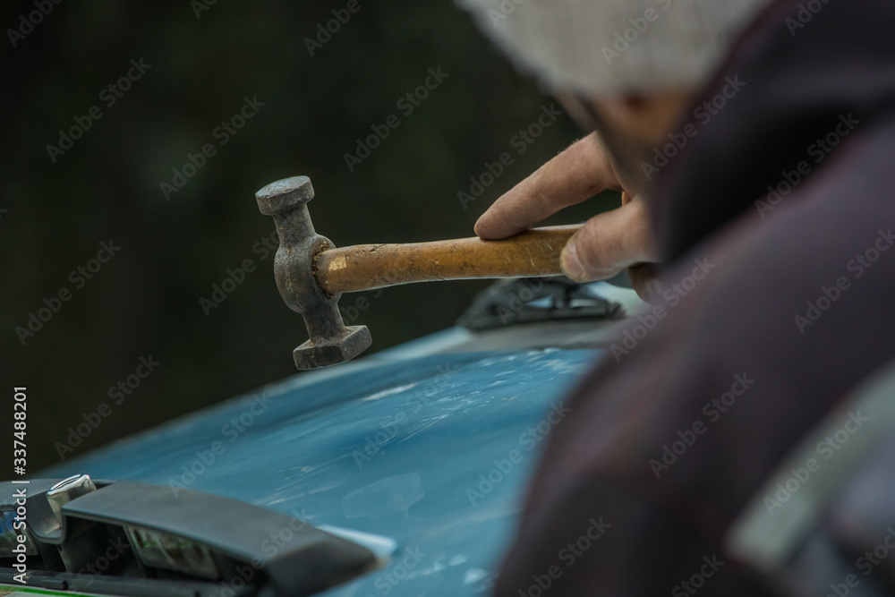 Auto repair worker straightening dents in metal car sheet or body using