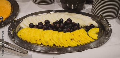 Different fruit like ananas, melon, orange and grapes on a stainless steel plate on buffet or party. Fresh fruit serving