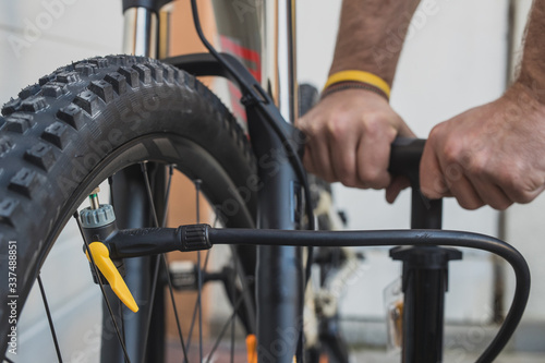 Obraz na płótnie Hands of a man seen pumping a bicycle tire using a stand alone hand pump. MTB tyre being pumped up outside of the house on an overcast day. w salonie