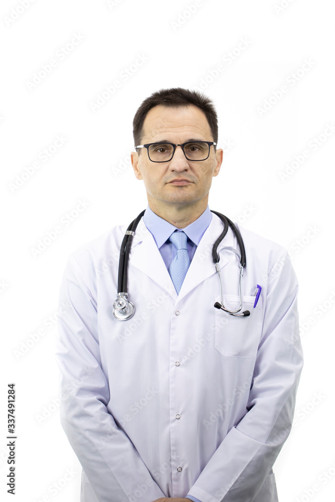 The therapist with glasses in a white coat with a stethoscope stands on a white background and looks at the camera. Medical worker. Serious look. Portrait of a doctor. Vertical shot. The therapist with glasses in a white coat with a stethoscope stands on a white background and looks at the camera. Medical worker. Serious look. Portrait of a doctor. Vertical shot.