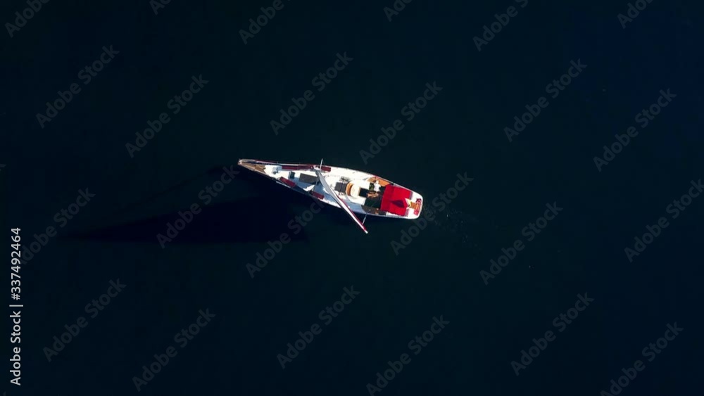 Top down drone shot of a yacht sailing through the deep blue ocean with the rippling light underneath Top down drone shot of a yacht sailing through the deep blue ocean with the rippling light underneath