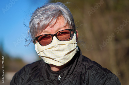 Elderly senior woman with gray hair wearing home made cloth face mouth nose virus mask outside. Can be used during coronavirus covid-19 outbreak prevention