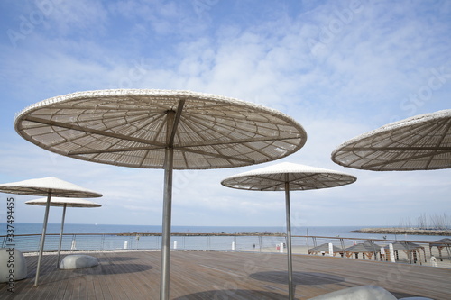 Fototapeta Naklejka Na Ścianę i Meble -  
White beach umbrellas on the background of the sea and blue sky. Cafe or space for relaxation. Space for text. Vacation and tourism concept