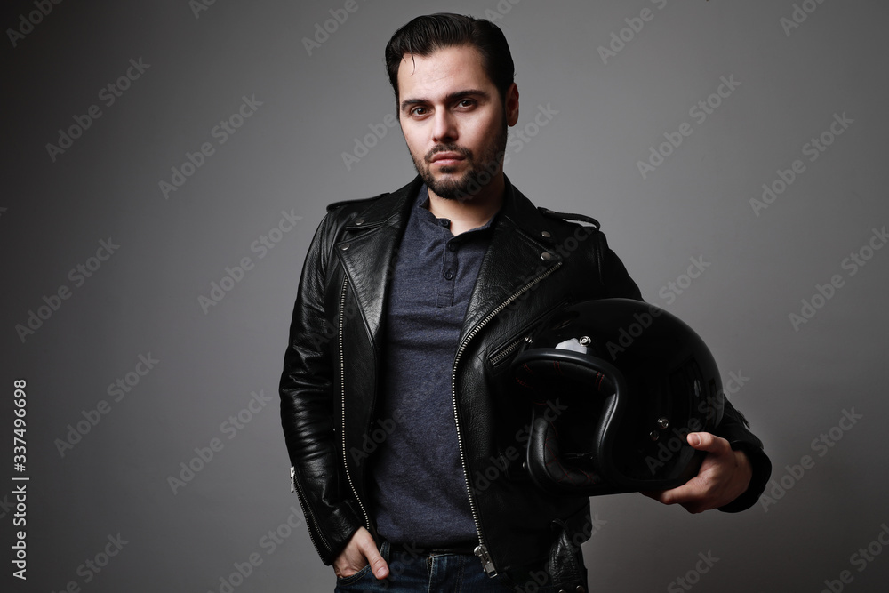 Fototapeta premium Bearded man wearing a black leather jacket holds helmet in his hands. Lifestyle, travel. Copy space.