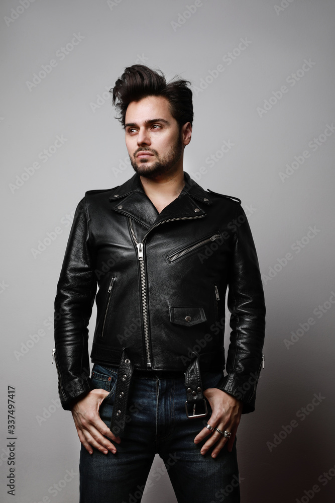 Fototapeta premium Fashionable handsome man in a leather jacket. Brutal bearded hipster in trendy leather biker jacket. Vertical.