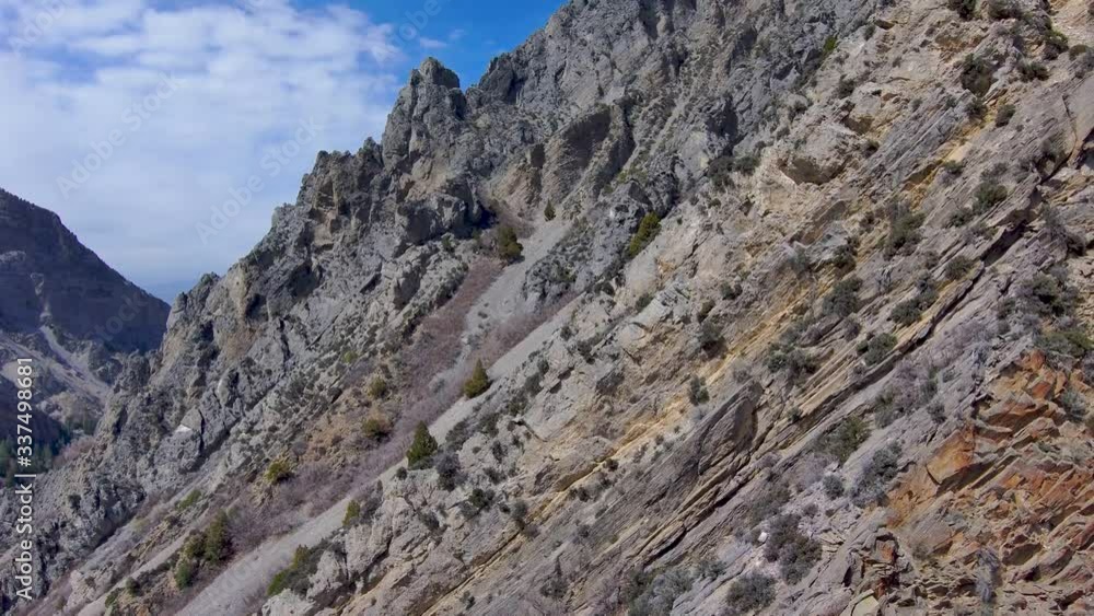 Flying backward beside a cliff in the Rocky Mountains with rugged geological strata in the landscape below - aerial Flying backward beside a cliff in the Rocky Mountains with rugged geological strata in the landscape below - aerial