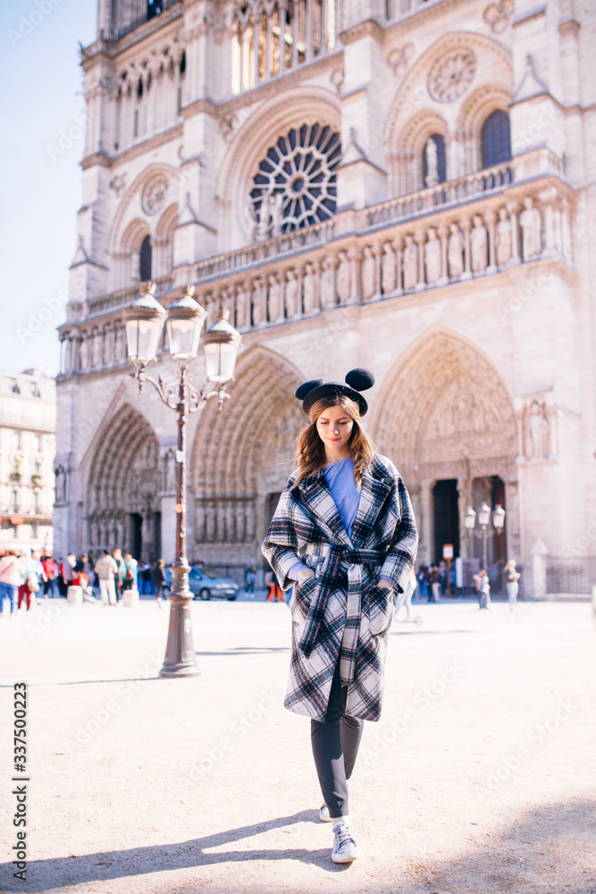 girl in a mikimaus hat in a beautiful coat on the background of the Parisian Cathedral of Notre Dame