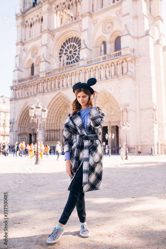 girl in a mikimaus hat in a beautiful coat on the background of the Parisian Cathedral of Notre Dame photo