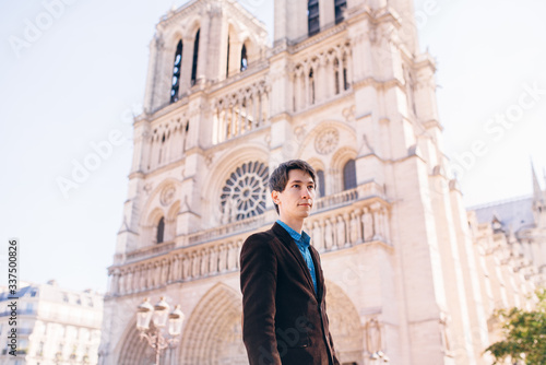 a young man poses against the backdrop of Notre Dame Cathedral in Paris.