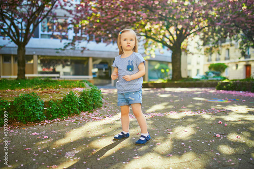 Cheerful two year old girl having fun in park with blooming cherry blossom trees