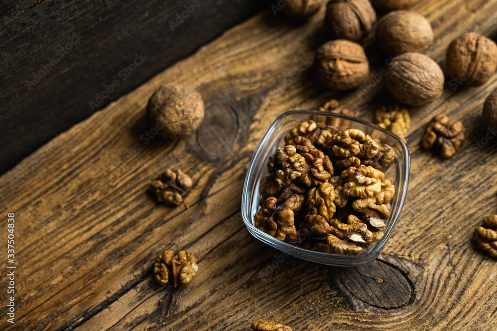 Walnut in a smale plate with scattered shelled nuts and whole nut which standing on a wooden vintage table. Walnuts is a healthy vegetarian protein nutritious food. Walnut on rustic old wood. Walnut in a smale plate with scattered shelled nuts and whole nut which standing on a wooden vintage table. Walnuts is a healthy vegetarian protein nutritious food. Walnut on rustic old wood.