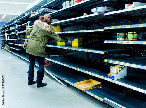 Foto Woman grabbing product of of thinly stocked shelves at a supermarket during the