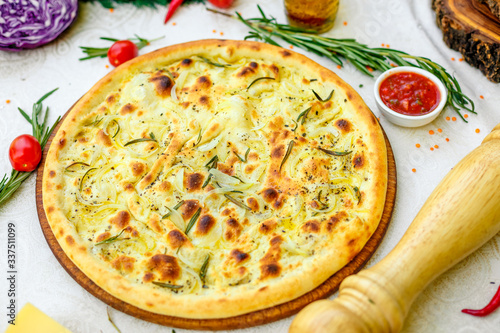 hot pizza with onions and basil on a wooden surface with vegetables on a white table