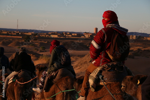 Viajero con turbante rojo viendo el atardecer, montando un camello en el desierto de Sahara en Marruecos 