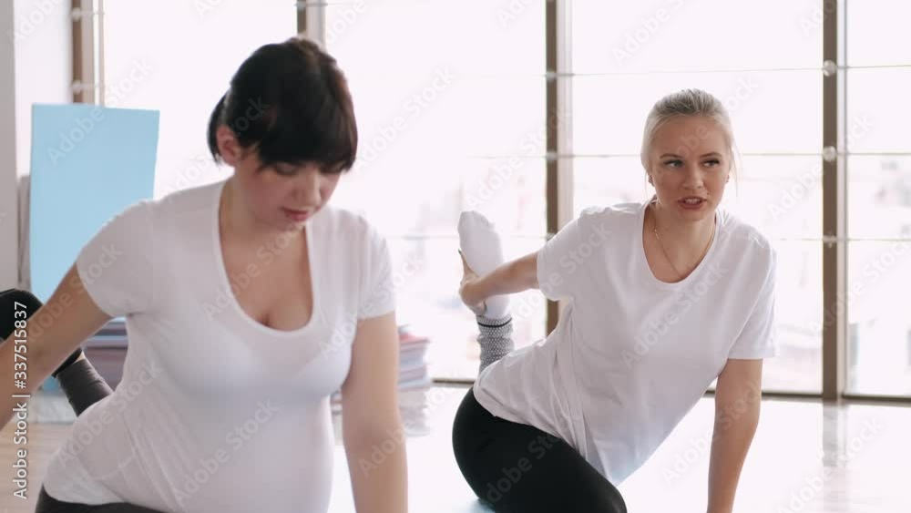 Pregnant woman are stretching legs with an instructor in a fitness gym. To be in tune with body pregnant women do prenatal exercises attending sport classes. Pregnant woman are stretching legs with an instructor in a fitness gym. To be in tune with body pregnant women do prenatal exercises attending sport classes.