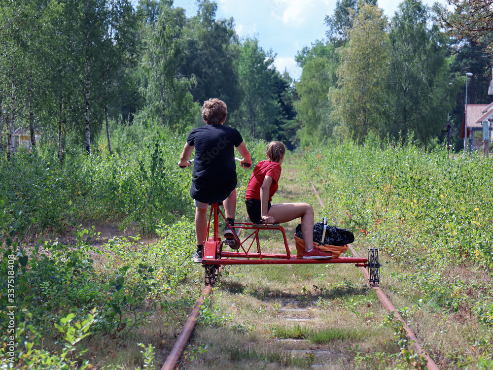 Boy and a girl are flying through the nature on a trolley. They are cycling in Sweden. Vehicle on a railroad. Boy and a girl are flying through the nature on a trolley. They are cycling in Sweden. Vehicle on a railroad.
