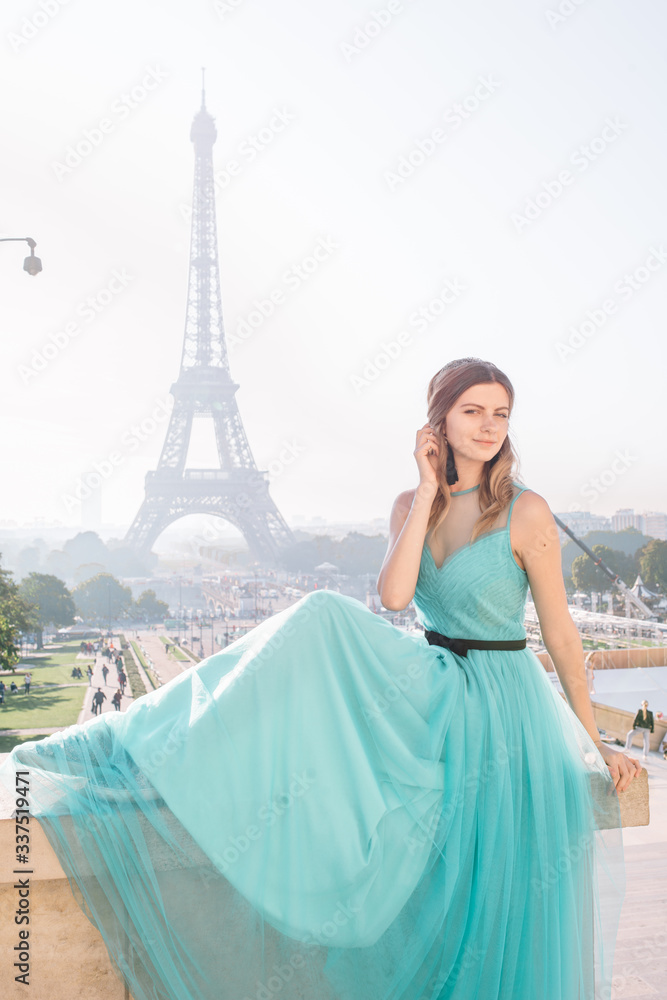 Beautiful girl in an azure evening dress in Paris with the Eiffel tower in the background.