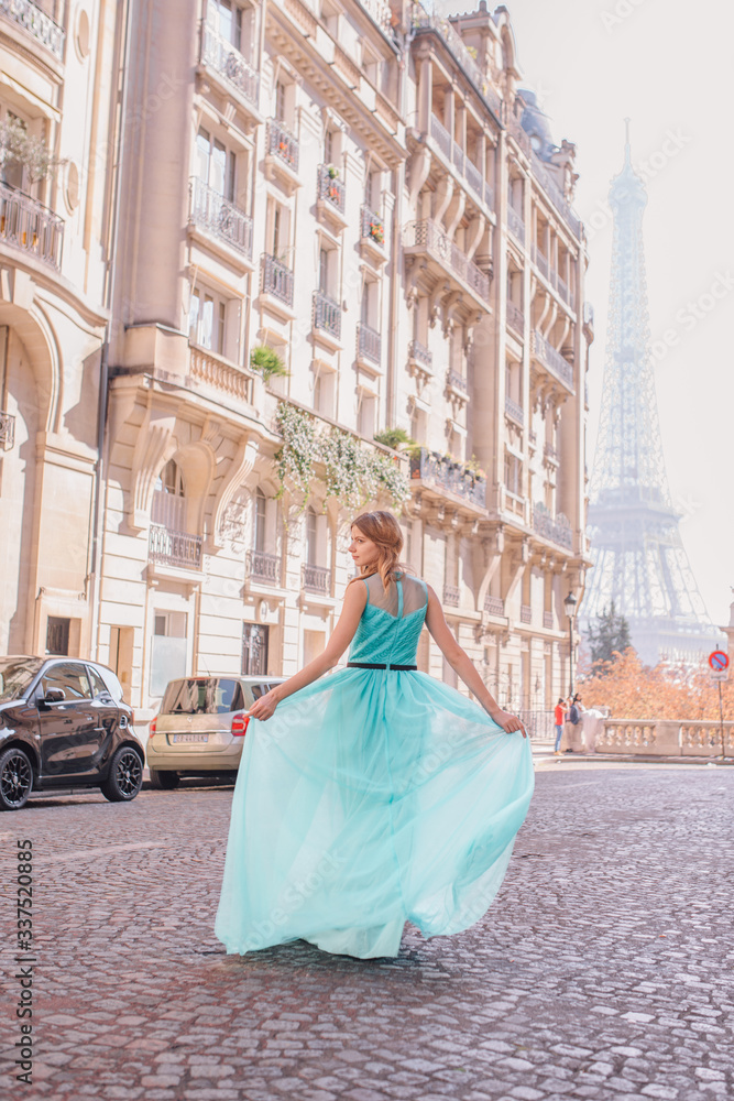 Obraz premium Beautiful young girl in a dress on the street with a view of the Eiffel tower