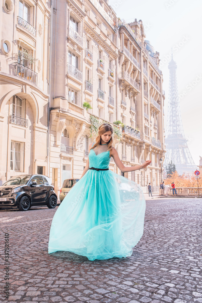 Fototapeta premium Beautiful young girl in a dress on the street with a view of the Eiffel tower