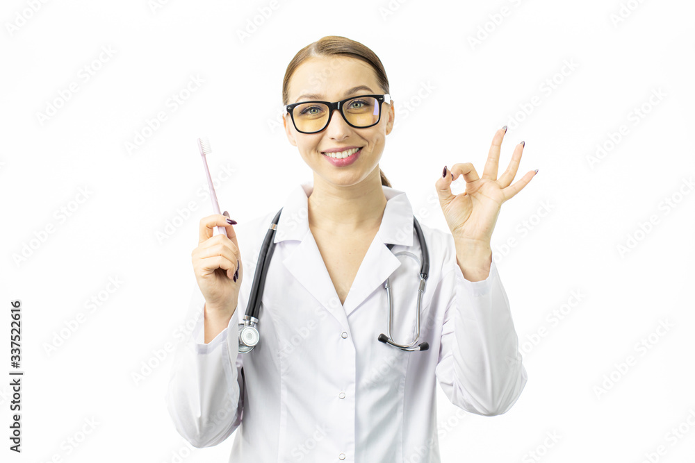 Portrait of sexy female dentist in white medical gown shows toothbrush and ok gesture. Shining snow-white smile. Stylish yellow glasses. White background. Dental treatment. Concept medical services. Portrait of sexy female dentist in white medical gown shows toothbrush and ok gesture. Shining snow-white smile. Stylish yellow glasses. White background. Dental treatment. Concept medical services.