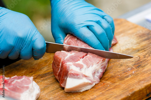 Close-up. A cook man in blue disposable gloves cuts a piece of red meat into pieces.