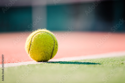yellow tennis ball on clay court on sunny day © Anastasia