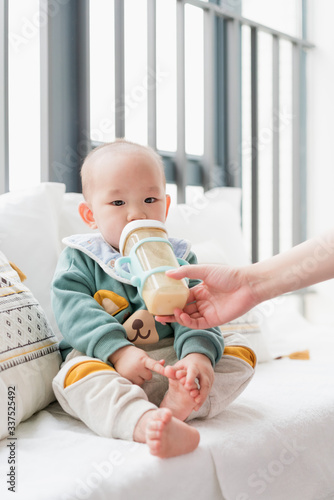 Asian baby sitting on a bay window and eating milk