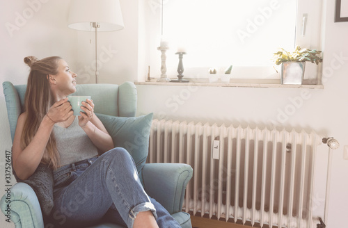 Junge Frau schaut aus dem Fenster und trinkt Tee