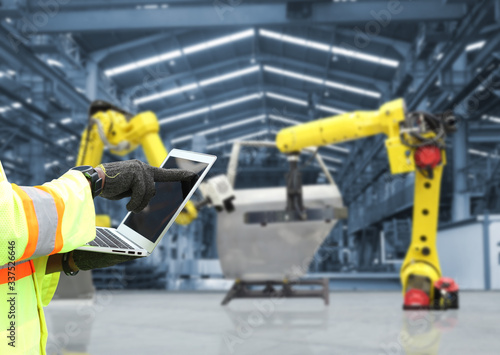 Man hand holding tablet or controller with automate wireless Robot arm in smart factory background. Mixed media of welding robot in the automotive parts industry