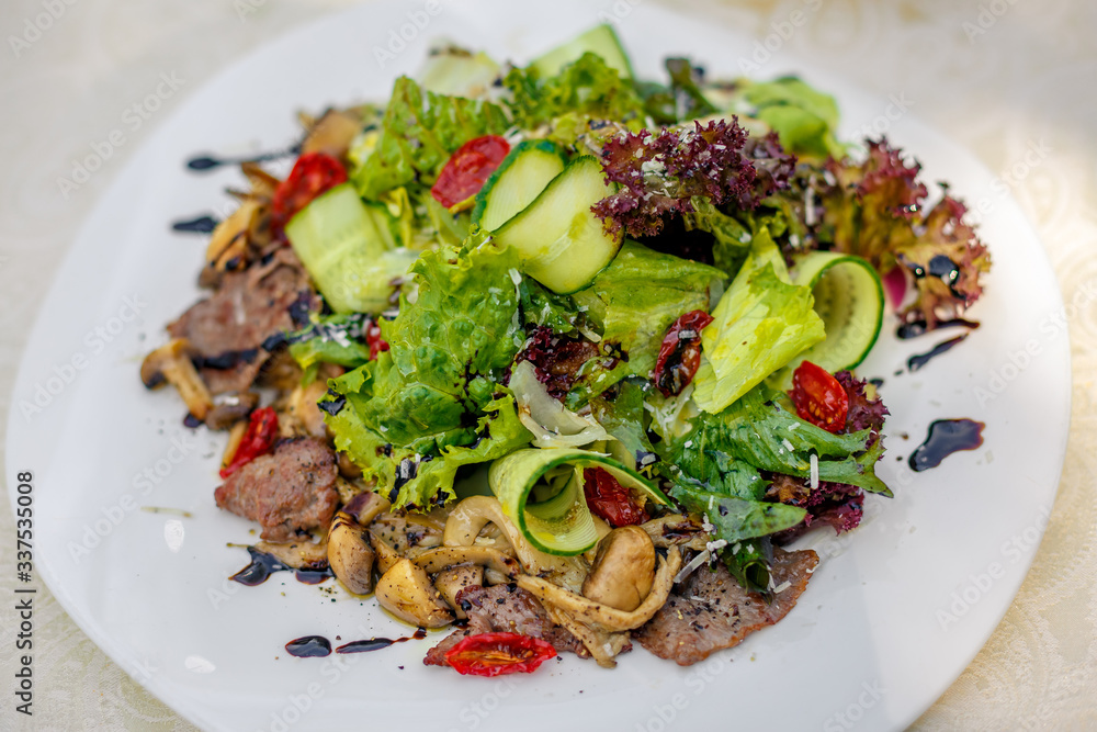 warm salad with meat, cucumber and vegetables on a white plate on the table