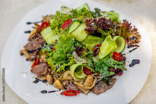 warm salad with meat, cucumber and vegetables on a white plate on the table