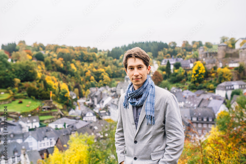 a man in a jacket stands against a panoramic view of Monschau, despite the wet weather. a man in a jacket stands against a panoramic view of Monschau, despite the wet weather.