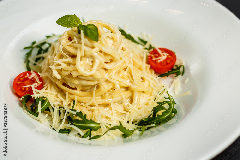 Tasty appetizing classic italian spaghetti pasta with tomato sauce, cheese parmesan and basil on plate on dark table