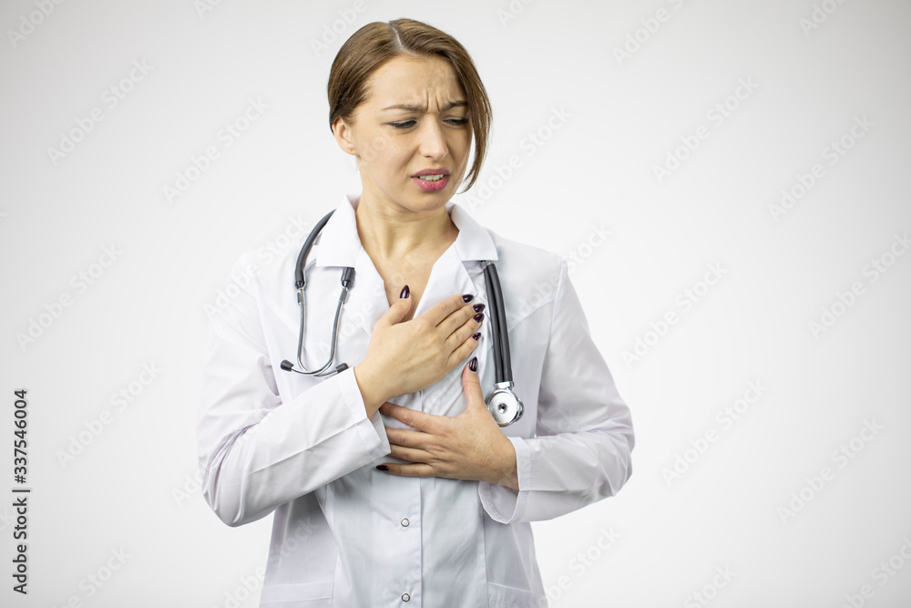 Sexy female surgeon suffers from severe heart pain. Heart attack. Adult caucasian doctor in a white coat with a stethoscope on his neck. Studio shot. White background Sexy female surgeon suffers from severe heart pain. Heart attack. Adult caucasian doctor in a white coat with a stethoscope on his neck. Studio shot. White background