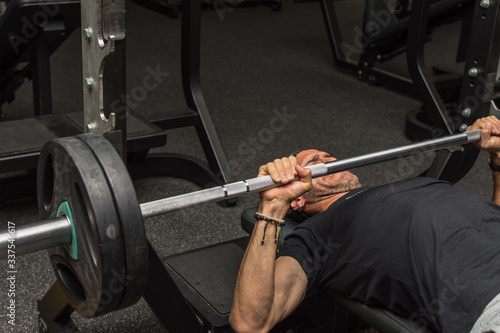 Sports young latin man lifting barbell in a gym. Gym chest exercises. Selective focus