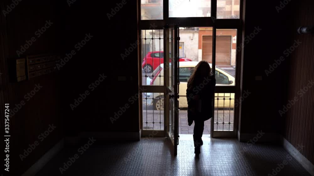 Silhouette of young attractive girl opening iron door with keys, entering to the hallway of dark modern residential building. Interior of hallway entrance Silhouette of young attractive girl opening iron door with keys, entering to the hallway of dark modern residential building. Interior of hallway entrance
