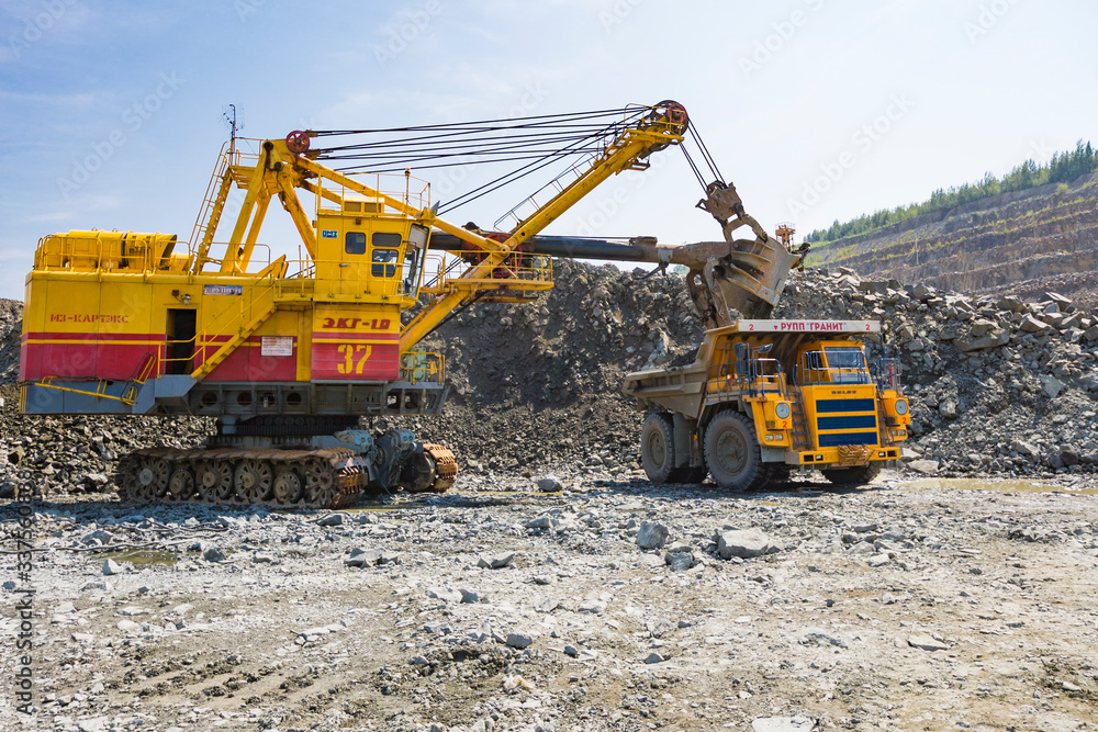 A mining excavator loads a huge truck with granite rock