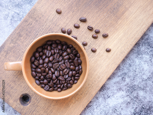 Roasted coffee beans in a brown cup on wooden over grey background with copy space for text. View from above..