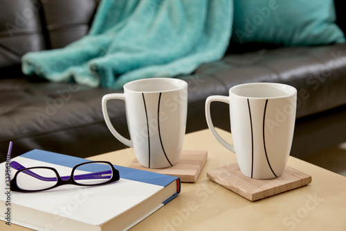 Two Mugs, a book and reading glasses on a table