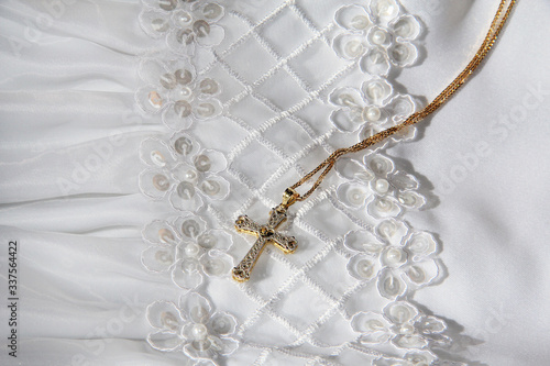 Gold cross necklace on top of fancy white satin communion dress/bridal gown with flower and pearl detail