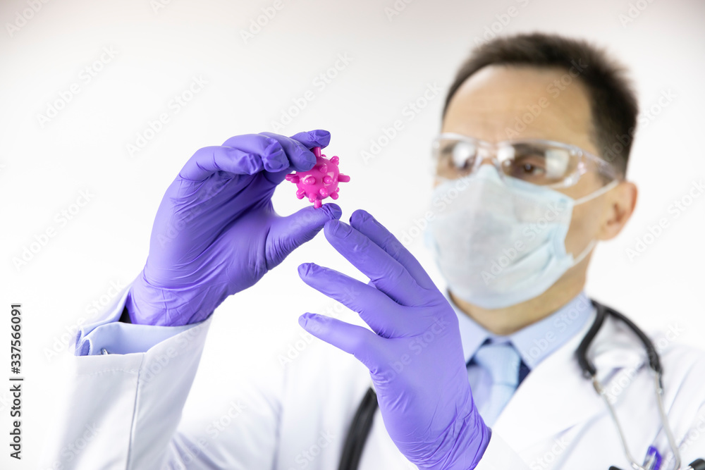 Male middle age lab technician assistant in medical uniform, protective mask and glasses looking at epidemic covid-19 virus cell in research laboratory, close-up, focused on coronavirus cell Male middle age lab technician assistant in medical uniform, protective mask and glasses looking at epidemic covid-19 virus cell in research laboratory, close-up, focused on coronavirus cell