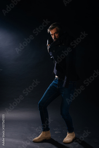Portrait of a formal dressed handsome adult man with grey hair posing inside a studio on a black background.. © qunica.com