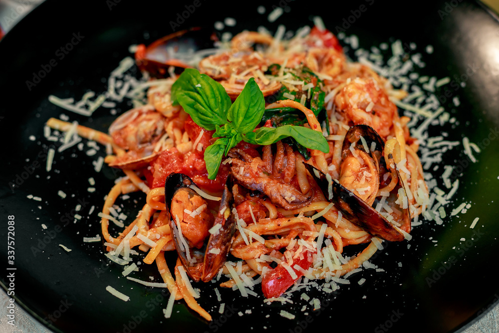 Italian pasta with parmesan cheese and seafood, with octopus, shrimps and mussels in a black plate on a white table Italian pasta with parmesan cheese and seafood, with octopus, shrimps and mussels in a black plate on a white table