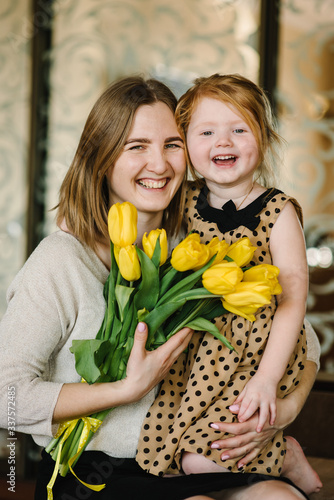 Happy mother's day. Daughter congratulates mom and gives her a bouquet of flowers tulips at home. Mom and child girl smiling, hugging. Family holiday and together.