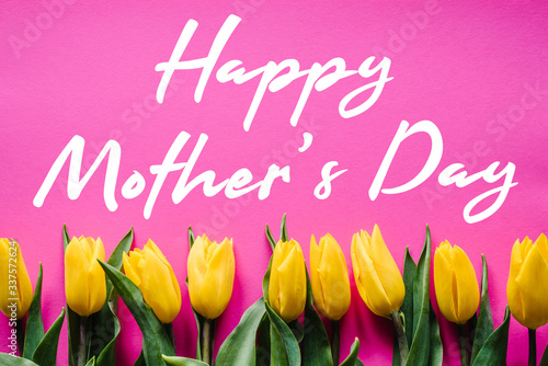 Happy mother's day. Text sign with yellow tulips on pink background. Floral greeting card concept. Sensual tender women image. Holiday greeting card for Mother's Day! Top view, flat lay.