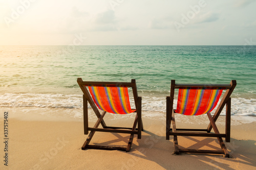 Two beach chairs on the sand beach with the light of the sun