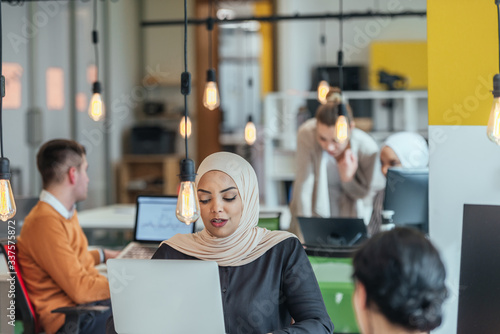 Billede på lærred African muslim girl wearing hijab working on a laptop in a modern startup company