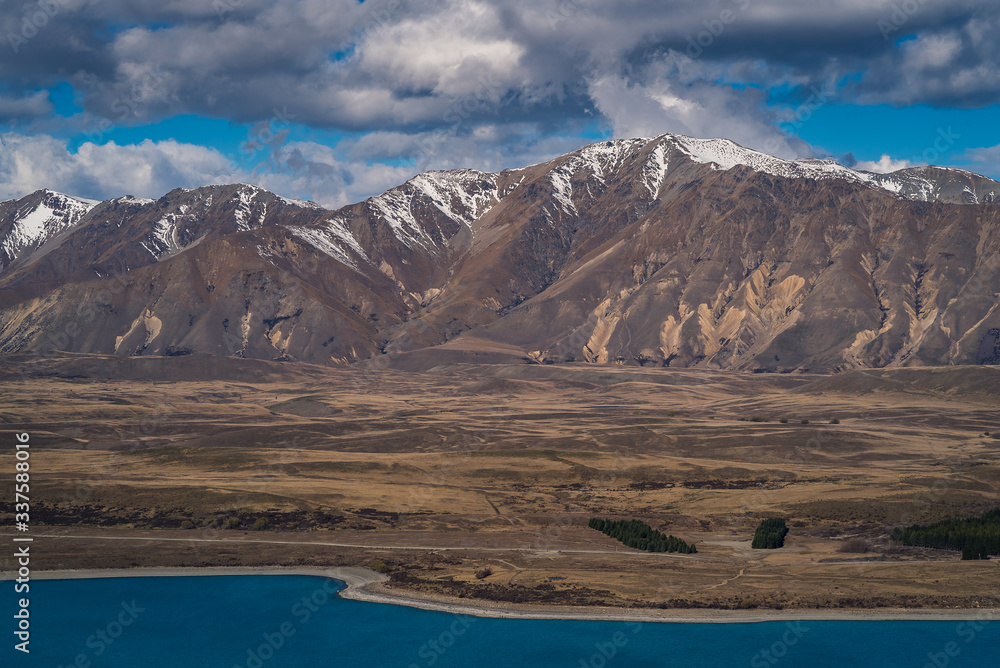 Scenic view from Mt St John Mountain Lake, with a view of the grassy hill, blue Lake Tekapo and the snow capped mountains in the background in Lake Tekapo in New Zealand South Island